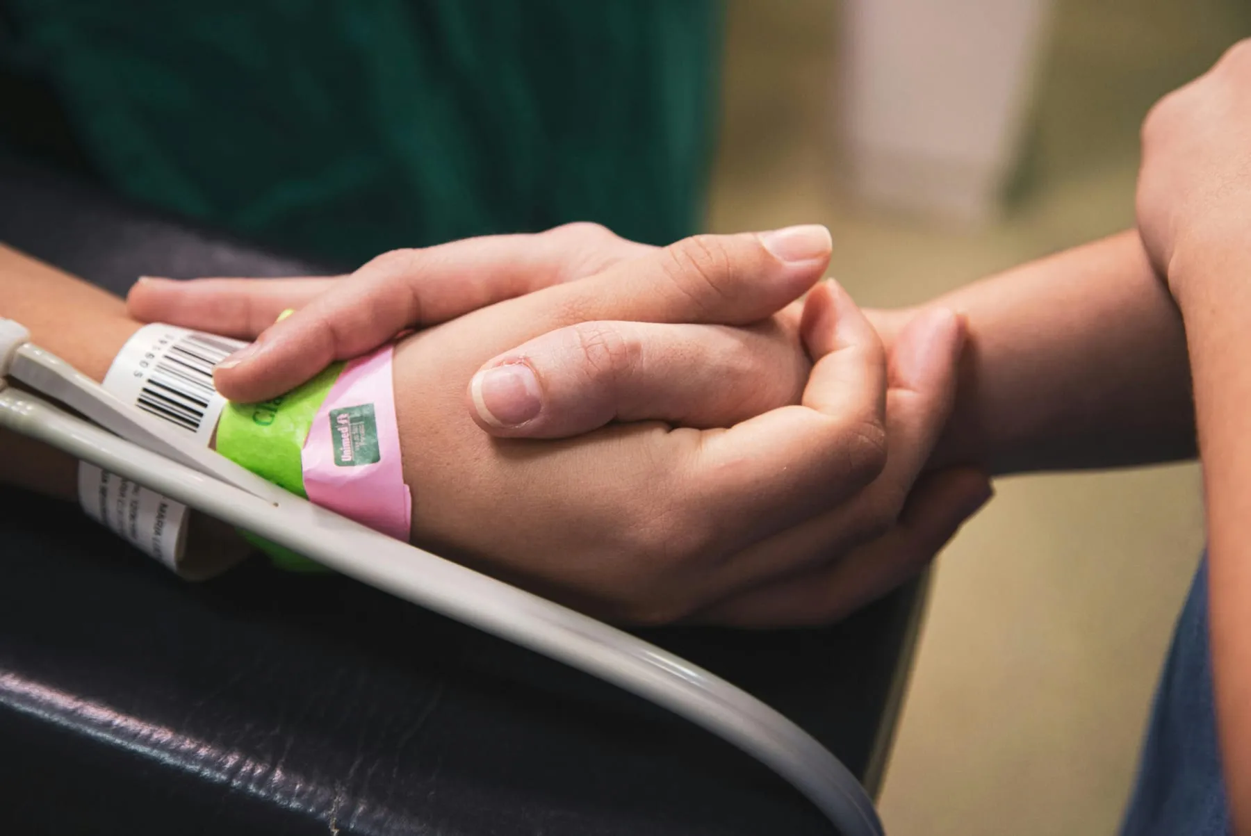 Dos manos sostienen la mano de una persona hospitalizada, con su brazalete de identificación.